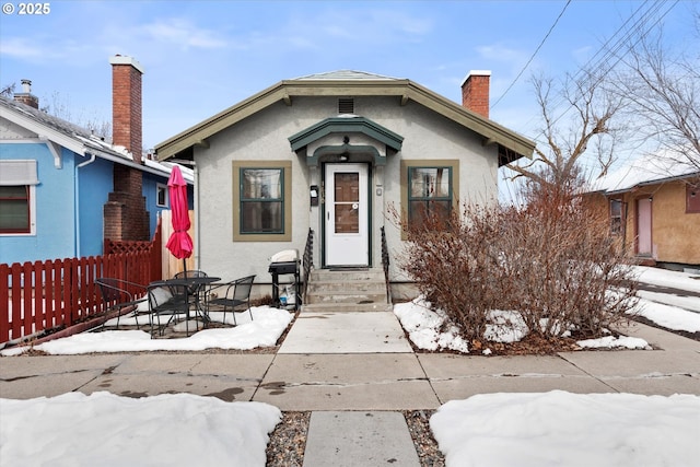 bungalow-style house with a chimney, fence, and stucco siding