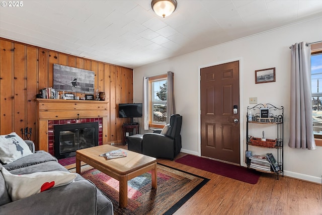 living room featuring a brick fireplace, wood walls, baseboards, and wood finished floors