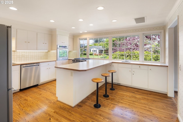 2160 Oakmont Way, Eugene, OR 97401 - kitchen featuring appliances with stainless steel finishes, ornamental molding, white cabinets, light wood-style flooring, and backsplash