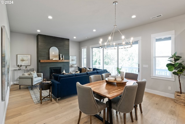 dining room with an inviting chandelier, light hardwood / wood-style flooring, and a large fireplace