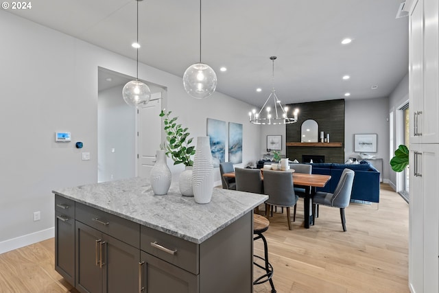 kitchen featuring hanging light fixtures, light stone countertops, white cabinets, a kitchen island, and light wood-type flooring