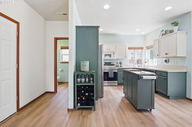 1146 SE Millright Ave, Mcminnville, OR 97128 - kitchen featuring stainless steel range with electric stovetop, white microwave, light wood-style flooring, a center island, and white cabinetry