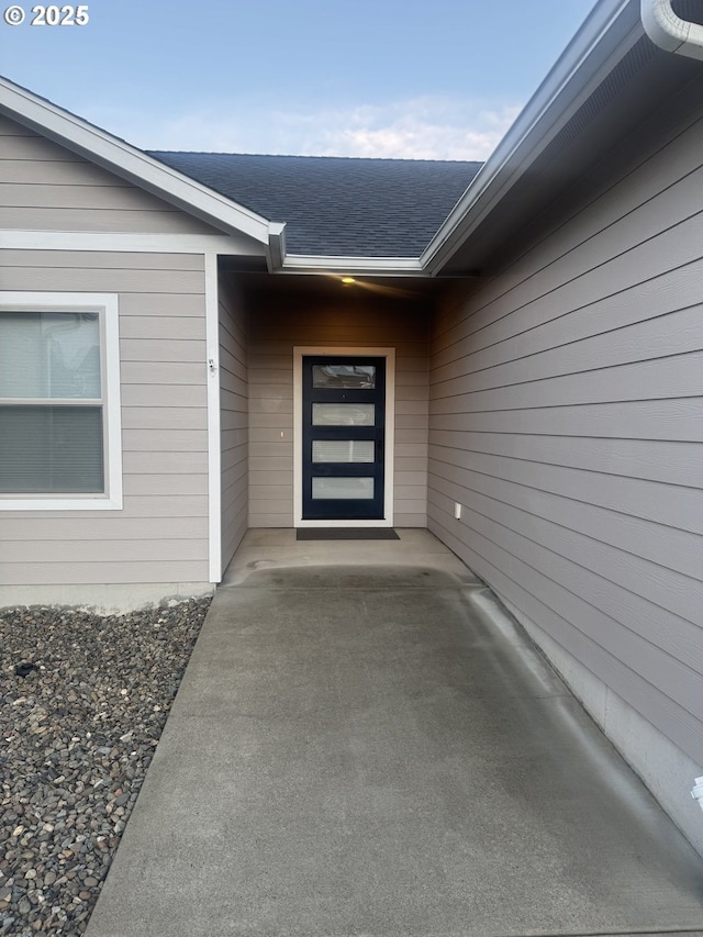 doorway to property featuring a patio area and a shingled roof