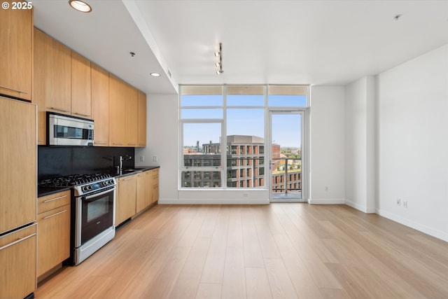 949 NW Overton St Unit 1007, Portland, OR 97209 - kitchen featuring appliances with stainless steel finishes, baseboards, light wood-style flooring, dark countertops, and track lighting