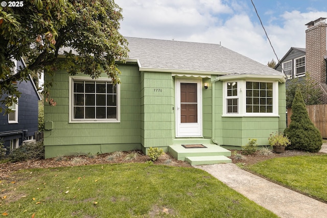 bungalow-style house featuring fence, a front lawn, and roof with shingles