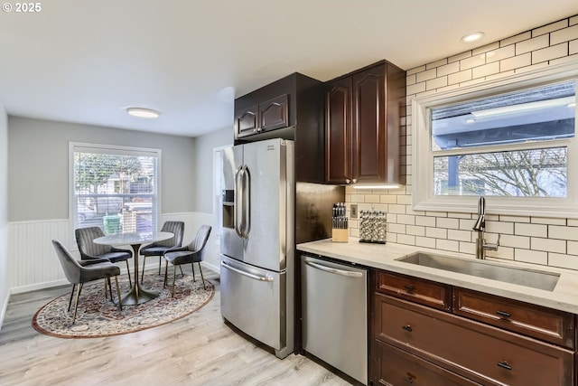 kitchen featuring dark brown cabinetry, sink, light wood-type flooring, appliances with stainless steel finishes, and backsplash