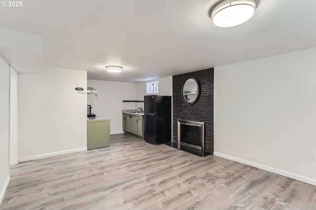 kitchen featuring a fireplace, light hardwood / wood-style flooring, sink, and black fridge