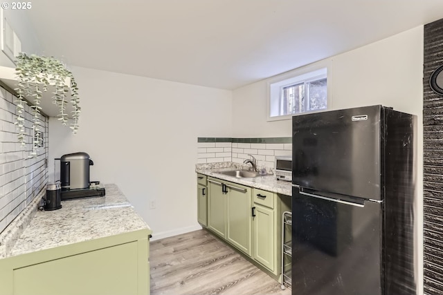 kitchen featuring sink, green cabinets, black refrigerator, decorative backsplash, and light wood-type flooring