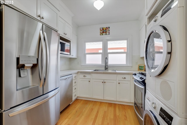 1534 NE 26th Ave Unit 8, Portland, OR 97232 - kitchen featuring appliances with stainless steel finishes, a sink, light wood-style floors, light countertops, and stacked washer and clothes dryer