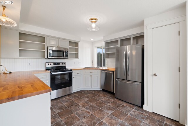 kitchen featuring open shelves, appliances with stainless steel finishes, a sink, wood counters, and stone finish floor