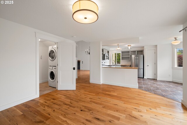 unfurnished living room featuring light wood-type flooring, stacked washer and dryer, and baseboards