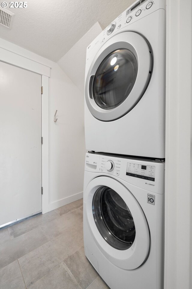 laundry area featuring visible vents, stacked washer and clothes dryer, laundry area, baseboards, and a textured ceiling