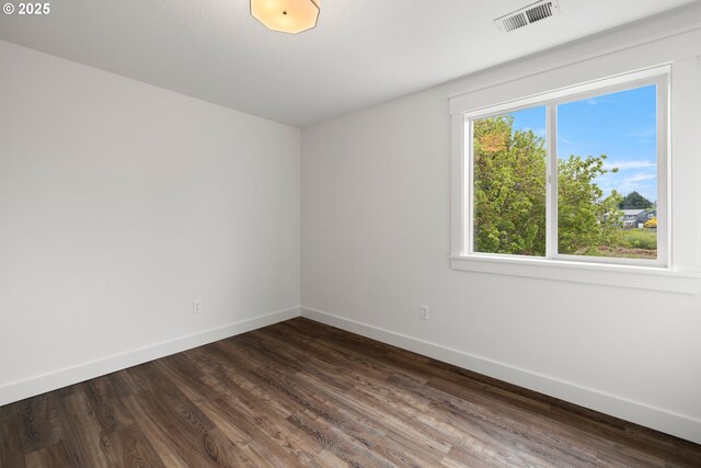 spare room featuring baseboards, visible vents, and dark wood-style floors
