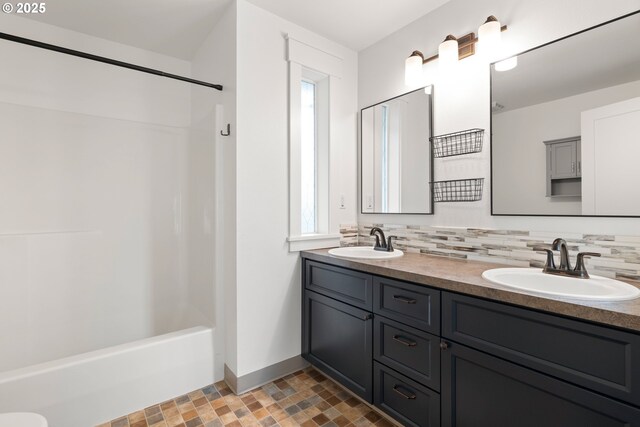 full bath with double vanity, tub / shower combination, a sink, and tasteful backsplash
