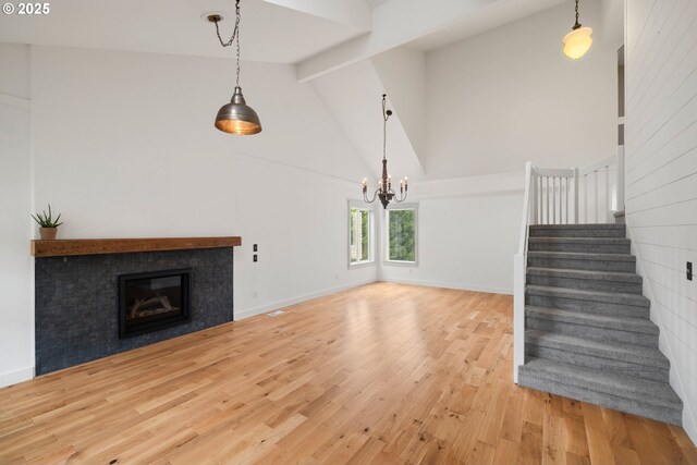 unfurnished living room featuring an inviting chandelier, beam ceiling, high vaulted ceiling, stairs, and wood finished floors