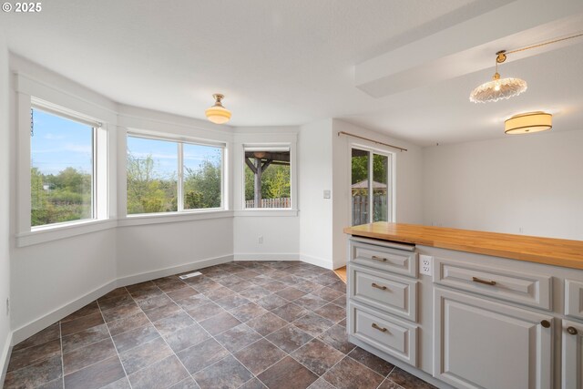 kitchen featuring stone finish floor, visible vents, baseboards, butcher block counters, and white cabinetry