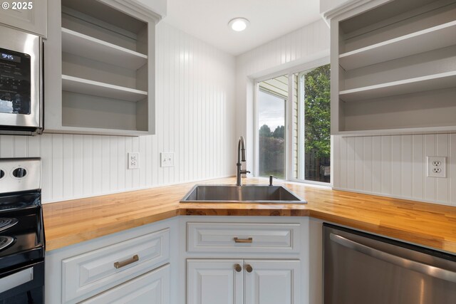 kitchen with a sink, open shelves, butcher block counters, and stainless steel appliances