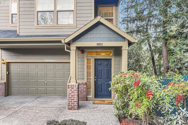 doorway to property featuring concrete driveway, a garage, brick siding, and roof with shingles