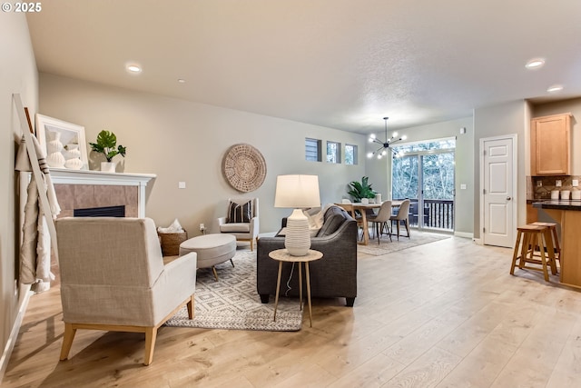 living area featuring an inviting chandelier, recessed lighting, light wood-type flooring, and a tile fireplace