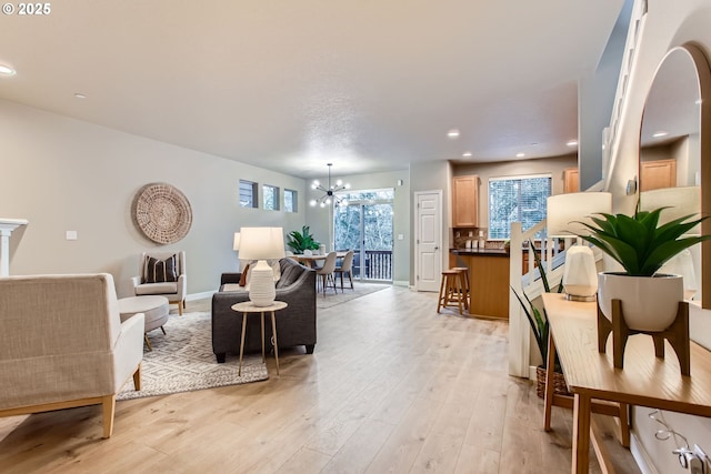 living area with recessed lighting, baseboards, an inviting chandelier, and light wood finished floors