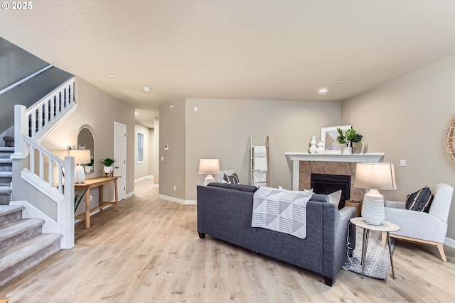 living room with a tile fireplace, baseboards, stairs, and light wood-style floors