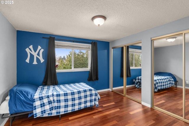 bedroom featuring multiple windows, dark wood-type flooring, two closets, and a textured ceiling