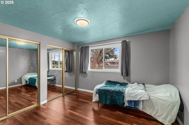 bedroom with a textured ceiling, dark hardwood / wood-style floors, and multiple closets