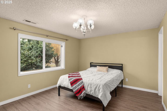 bedroom featuring an inviting chandelier, hardwood / wood-style flooring, and a textured ceiling