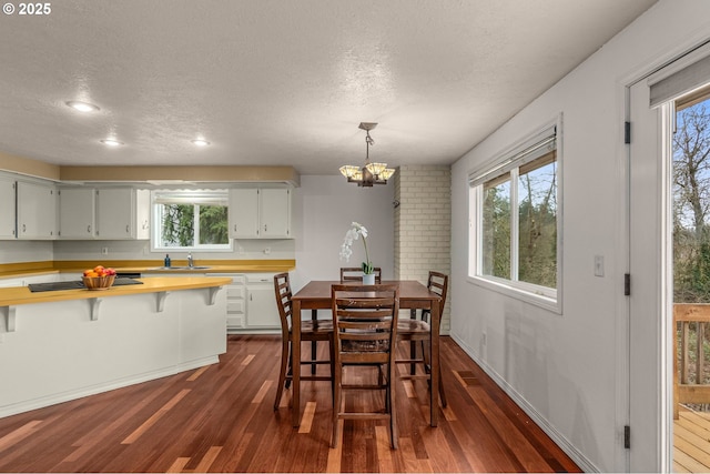 dining room featuring an inviting chandelier, a healthy amount of sunlight, dark hardwood / wood-style flooring, and a textured ceiling