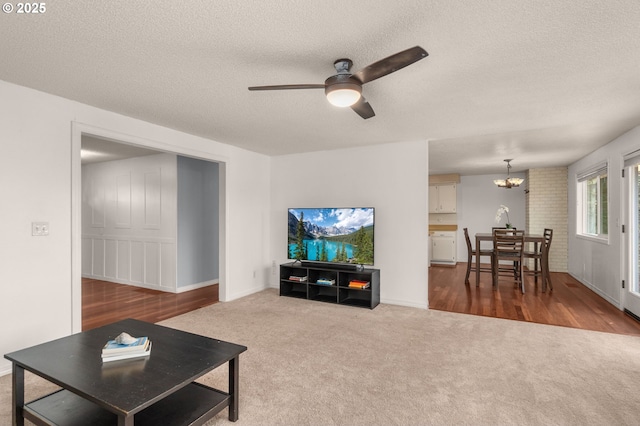 carpeted living room featuring ceiling fan with notable chandelier and a textured ceiling