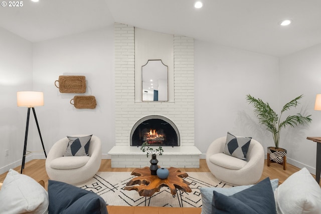 living room featuring vaulted ceiling, a brick fireplace, and light wood-type flooring