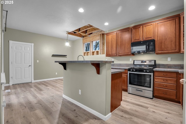 kitchen featuring a kitchen breakfast bar, light wood-type flooring, stainless steel gas range oven, pendant lighting, and a center island