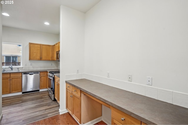 kitchen with wood finished floors, recessed lighting, built in desk, a sink, and appliances with stainless steel finishes