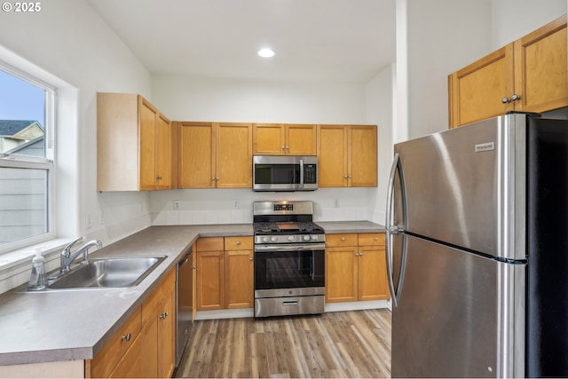 kitchen featuring brown cabinets, a sink, light wood finished floors, stainless steel appliances, and recessed lighting