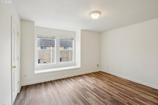 unfurnished room with a textured ceiling, baseboards, and wood finished floors