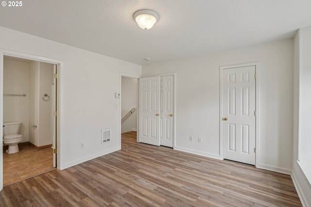 unfurnished bedroom with baseboards, two closets, wood finished floors, and connected bathroom