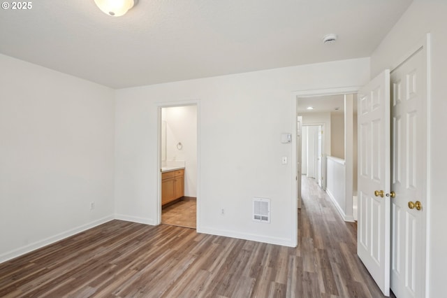 unfurnished bedroom featuring baseboards, ensuite bathroom, wood finished floors, and visible vents