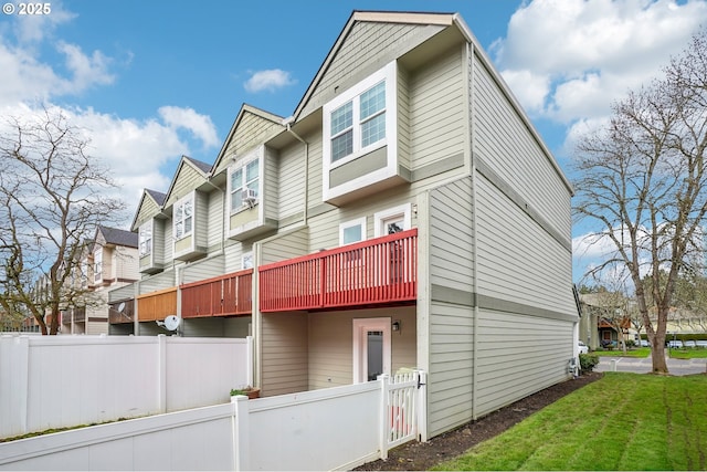 back of property featuring a residential view, fence, cooling unit, a balcony, and a yard