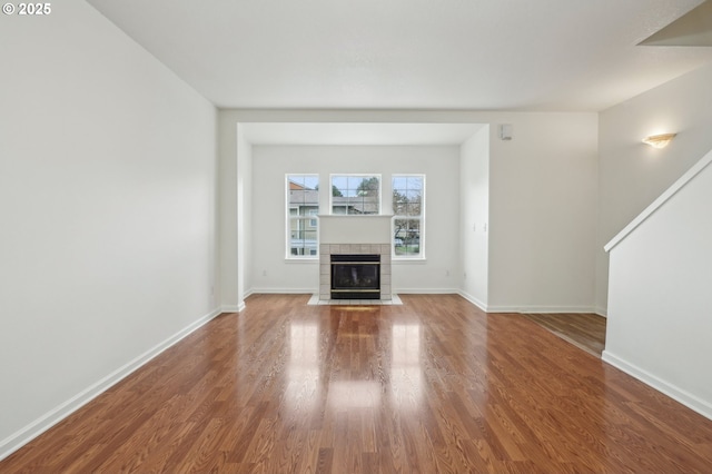 unfurnished living room with baseboards, wood finished floors, and a tile fireplace