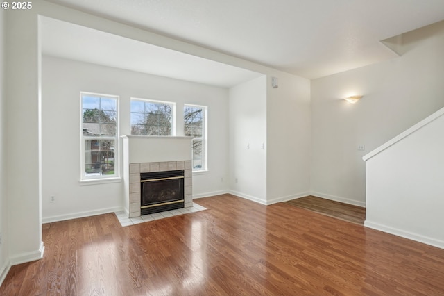 unfurnished living room with a tiled fireplace, baseboards, and wood finished floors