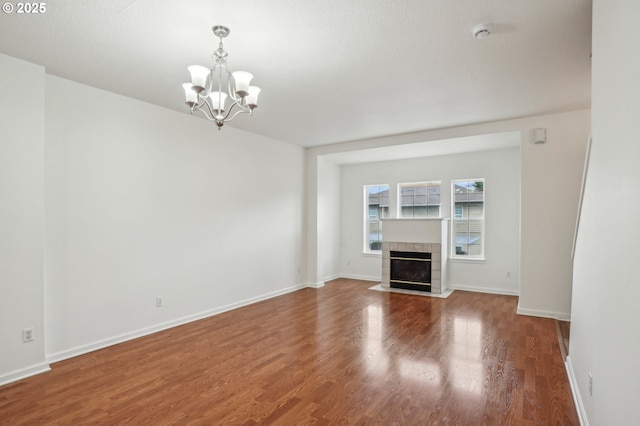 unfurnished living room featuring baseboards, wood finished floors, a chandelier, and a fireplace