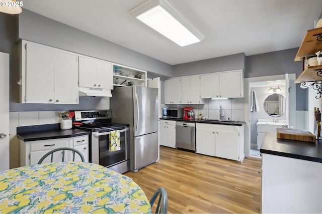 kitchen with appliances with stainless steel finishes, under cabinet range hood, dark countertops, and light wood-type flooring