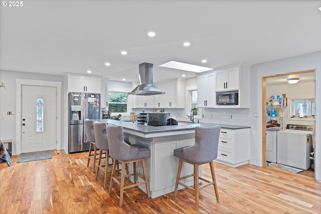 kitchen with island exhaust hood, stainless steel refrigerator with ice dispenser, washing machine and clothes dryer, a sink, and black microwave