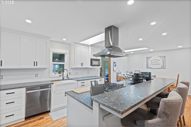 kitchen featuring a breakfast bar, island exhaust hood, stainless steel dishwasher, a sink, and built in microwave