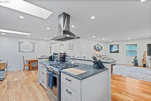 kitchen with light wood-style flooring, a kitchen island, white cabinets, stainless steel range with gas cooktop, and island exhaust hood