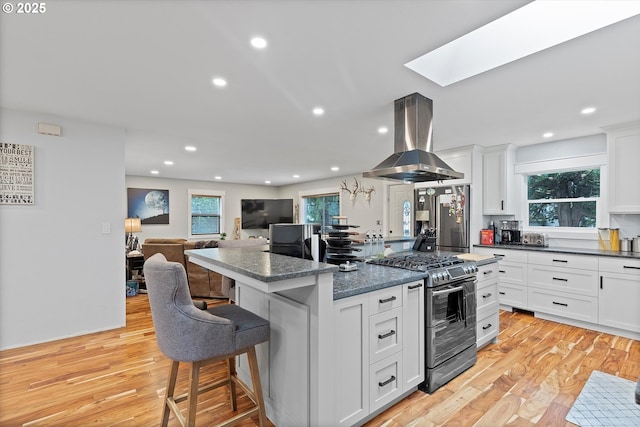 kitchen with light wood-style floors, appliances with stainless steel finishes, island range hood, and a breakfast bar