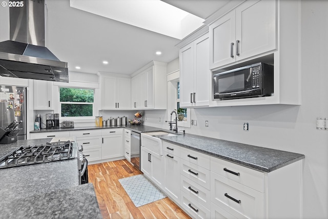 kitchen featuring light wood-style floors, stainless steel appliances, wall chimney range hood, white cabinetry, and a sink