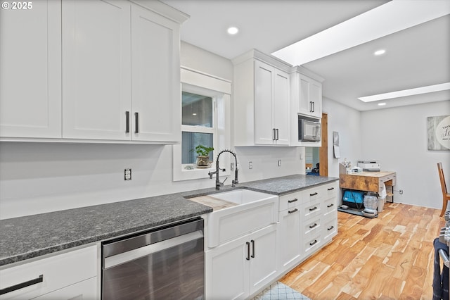 kitchen with black microwave, light wood-style flooring, beverage cooler, a sink, and white cabinetry