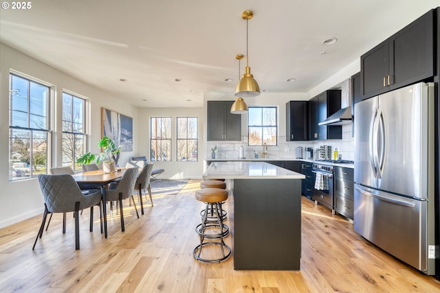 kitchen with stainless steel appliances, light countertops, dark cabinetry, a center island, and decorative light fixtures