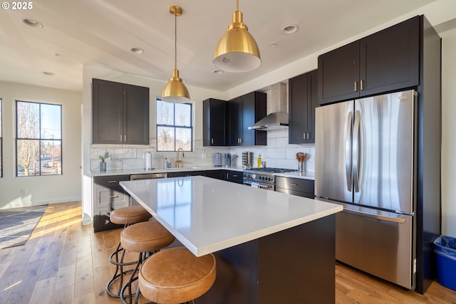 kitchen featuring stainless steel appliances, light countertops, a kitchen island, and wall chimney range hood